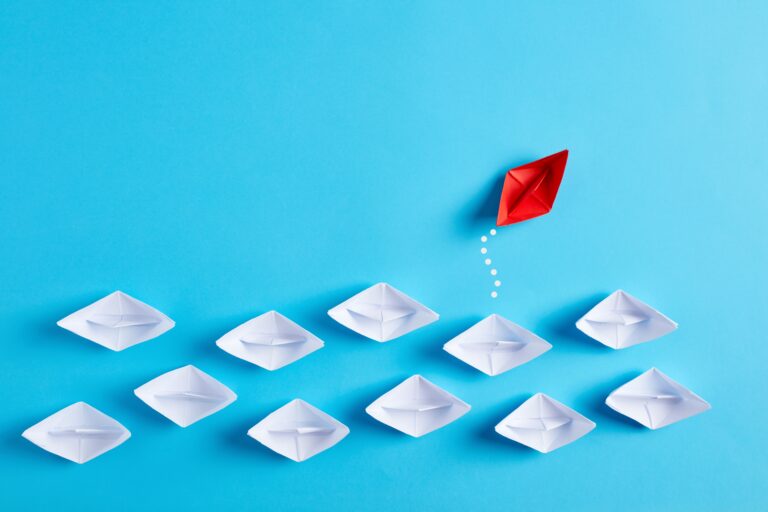 White paper boats in a row with one red boat going in the different direction